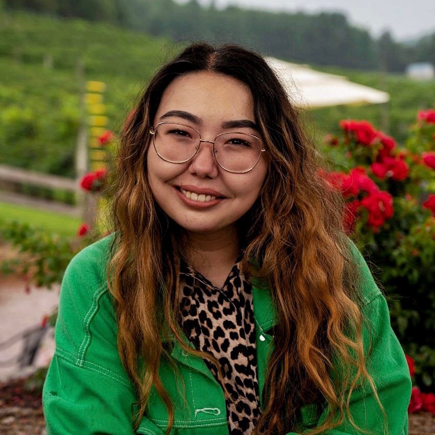Alt text: The picture of Sabina smiling in Madison, WI. She is wearing a green jacket and round glasses. Image credit: Luke Davies.